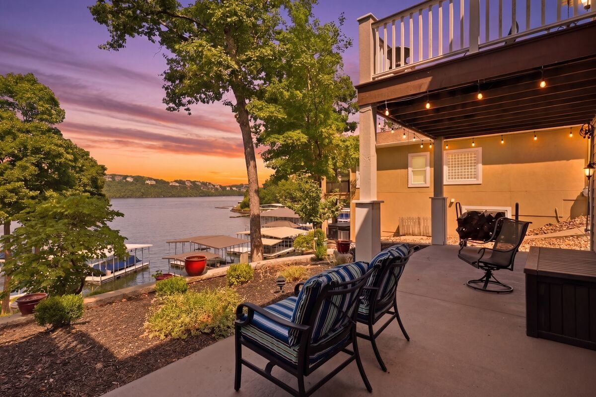 Covered lakeside patio with cozy seating, string lights, and stunning sunset views over Lake of the Ozarks.